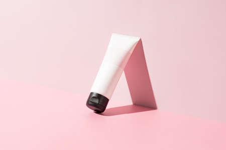 Empty white cosmetic tube for face cream, body lotion, facial cleanser or shampoo on a bright pink background with sunlight and shadows. Skin care cosmetics mockup.の写真素材