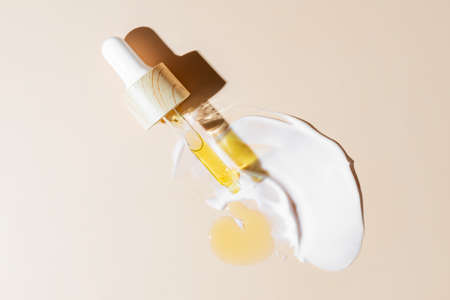 yellow beauty face oil dripping from bamboo dropper on beige background. Skin care cosmetic...