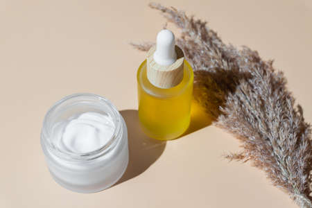 close up of collagen cream in glass jar, serum in a glass bottle and dry flowers reeds on beige background. Set for skin and body care beauty products.の写真素材