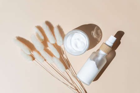 Face and eye moisturizer cream and serum in a glass bottle and jar and dried herb on light beige background. Concept eco organic natural cosmetic products for skincare.の写真素材