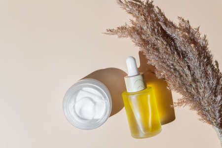 anti-aging retinol facial serum in a glass bottle and face cream on beige background with copy...