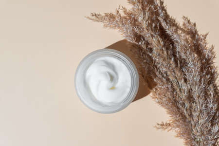 top view of face cream on beige background. Dry ear reeds or pampas grass decoration. Professional...