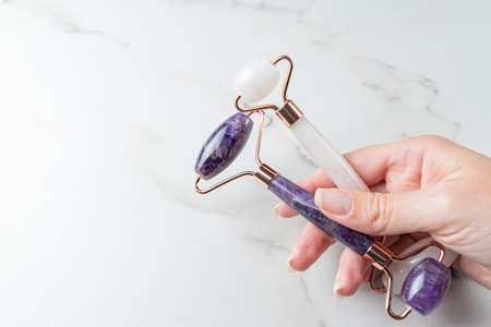Female hand holding Rose quartz and amethyst face rollers for beauty facial massage therapy. Skin...