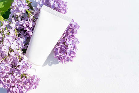 Top view of face or hand cream in squeeze package, cosmetic tube with pink lilac flowers on a wooden white background. Cosmetics spa branding mockup, flower flat lay. copyspace.の写真素材