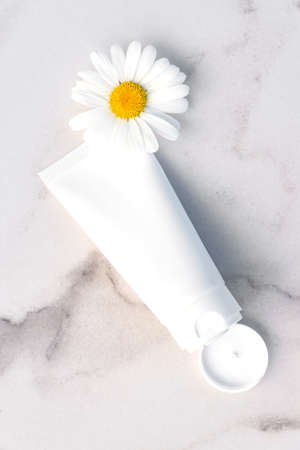 Natural skincare product branding mock up. Blank white squeeze plastic tube on marble background with camomile flower. Packaging of cream, body lotion, gel or facial foam. beauty cosmetic conceptの写真素材