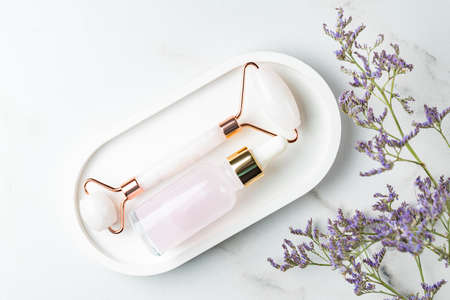 skincare concept. Bottle of cometic product, serum or oil. Quartz roller face massage. Cosmetics and tools on ceramic tray on marble background with copy sapceの写真素材