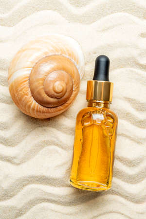Glass bottle with serum cosmetic product on the background of seashells and sea beach sand. product presentation on a sandy background. unbranded mockup.の写真素材