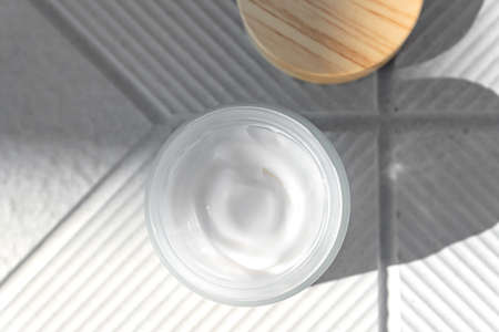 Top view of open glass jar with face cream with peptides for anti aging effect on concrete...