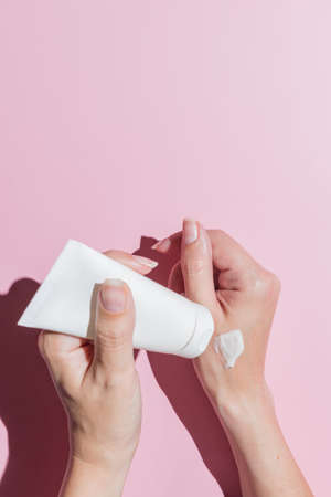 Woman squeezes the cream out of the tube. Female hands with a white tube on a pink background close-up. skincare cosmetics.の写真素材