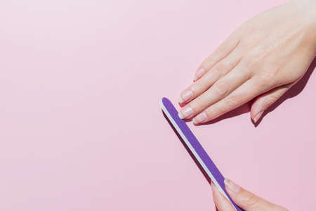 woman filing her nails with purple fimger file, making manicure at home, hands care, time for yourself concept. pink background. top view.の写真素材
