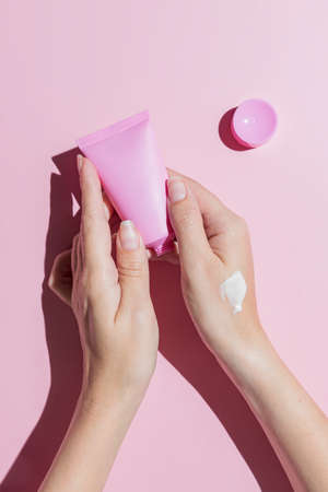 Young woman hands holding pink cream tube and applying cream. Skin care and body treatment. Trendy shoot in modern style. Pink background and hard shadows.の写真素材