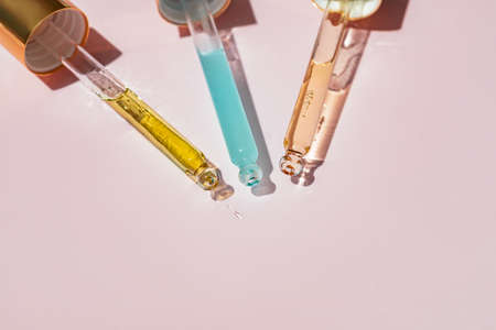 Three Pipettes with essential oil or beauty serum for face and body skin care on pink background with space for textの写真素材
