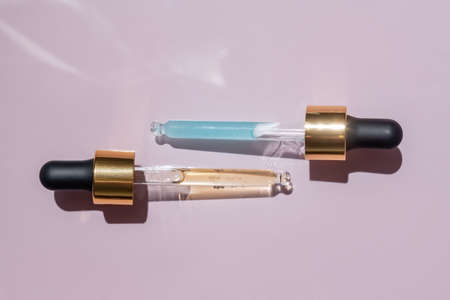 Transparent pipettes with blue and yellow cosmetics serum on a light pink background. product texture. Dropper glass bottle branding mockup. cosmetic pipette.の写真素材
