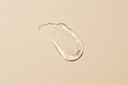 Squeezed cosmetic clear cream gel texture Iisolated on beige background. Close up transparent serum...