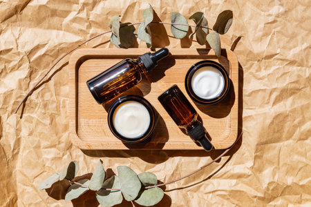 Dark glass cosmetic bottles with a dropper and face cream on a craft paper background with eucalyptus leaves. Natural cosmetics concept, natural essential oil and skin care products.の写真素材