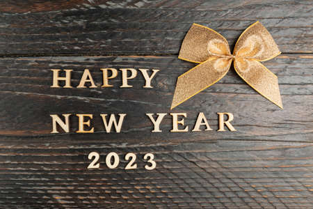 Happy new year greeting card. gold ribbon tied in a bow and wooden text happy new year 2023 on festive wooden tableの写真素材