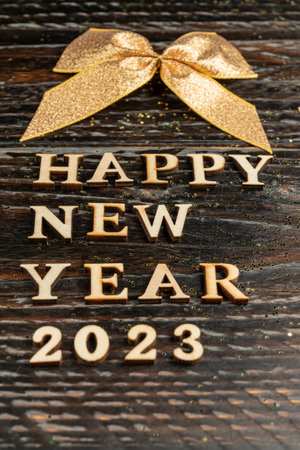 Happy new year 2023 greeting card. Wooden letters and golden bow on dark wooden backgroundの写真素材