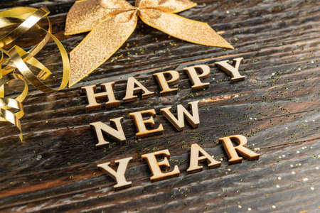 Happy new year wooden taxt on dark wooden background with golden tied bow and scattered confetti. New year greeting card.の写真素材