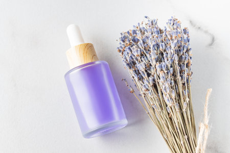 Bottle of essential oil and lavender flowers on white marble backgroundの写真素材