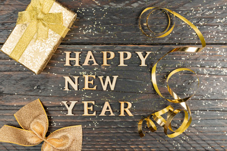 Festive greeting card with happy new year text on wooden bakground with gold sparkling confetti and present boxの写真素材