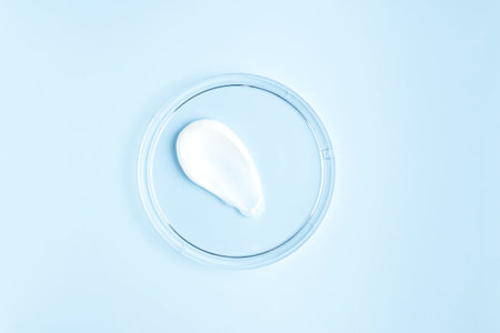 White cosmetic face cream or body lotion moisturizer strokes on pastel blue background in petri dish. Hygiene, skincare product with creamy texture. Beauty face creme smear swatch on color backgroundの写真素材