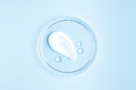 smear of cream stroke and round transparent drops of gel serum in a petri dish on a blue background. Concept laboratory tests and research, making and testing cosmeticの写真素材