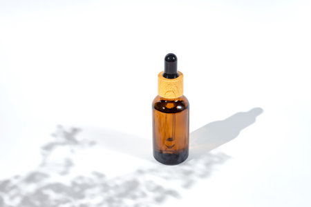 Amber dropper bottle with serum or gel on white background with daylight with beautiful flowers shadows. Skincare natural cosmetic.の写真素材