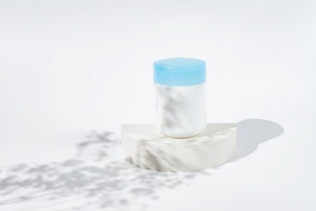 Cosmetic jar for cream on white podium and spring flowers shadows. Template for branding identity for cosmetics produce.の写真素材