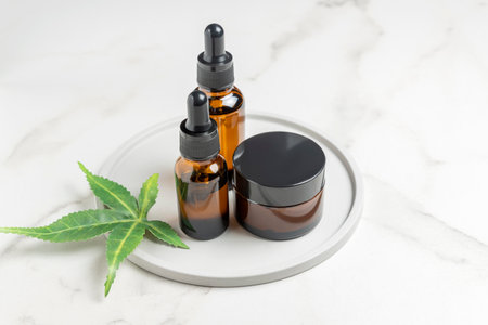 Cannabis face cream and serum or oil dropper concept. natural cosmetic. CBD oil, THC tincture and hemp leaves on a marble table backgroundの写真素材