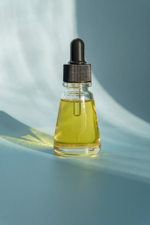 A glass dropper bottle with beauty care serum, AHA acid and vitamins on blue background with trendy...