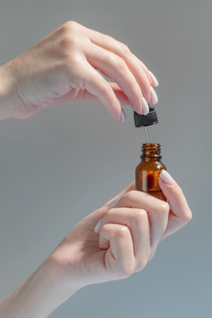 female hand with Dropper of essential oil, aromatherapy essence, beauty serum or medicinal liquid on beige background. Unbranded bottles for your designの写真素材
