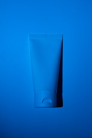 Plastic white tube on neon filter blue background. Skincare cleansing cosmetic. beauty concept face body careの写真素材