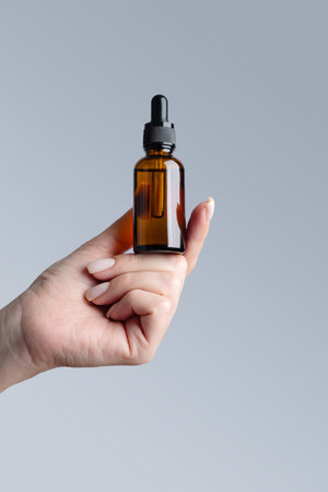 Beautiful groomed woman's hand with amber glass serum bottle mock up on a gray background.の写真素材