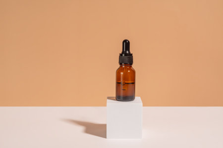 Dark glass cosmetic bottle with a dropper on a white cube podium on beige background. Natural cosmetics concept, natural essential oil and skin care productsの写真素材