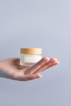 Hand holding blank white matte glass cream jar with bamboo lid on gray background. Cosmetic beauty product branding mockup. skincareの写真素材