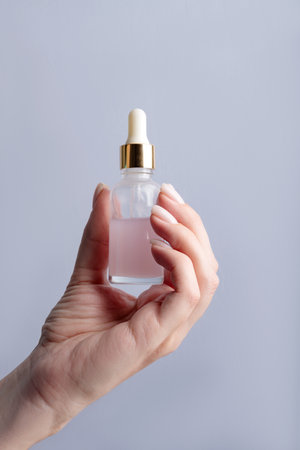 Female hand holding a bottle with serum for face care. Daily routine and treatment for the skin. Mockup for your designsの写真素材