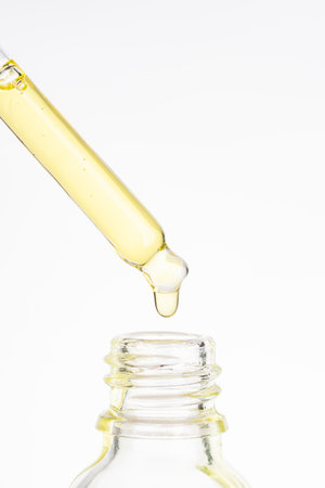 Cosmetic pipette with yellow oily drop close up on white background. Beauty drop of luxurious gold...