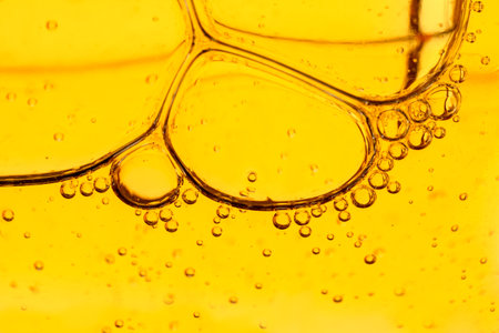Golden yellow abstract oil bubbles or face serum background. Oil and water bubbles macro photography
