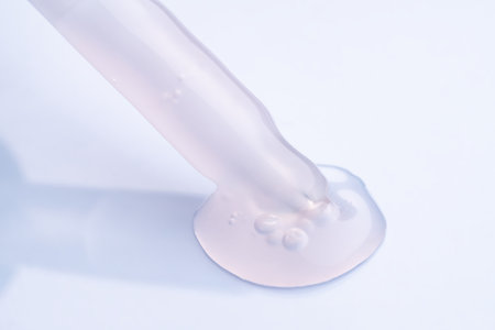 Pipette with cosmetic product in water with bubbles. Pink face oil on blue background.の写真素材