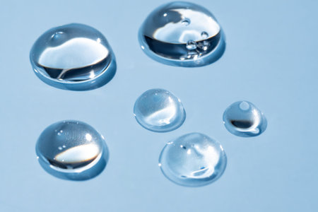 Pure transparent cosmetic gel drops on blue background, skin care glycerin texture.