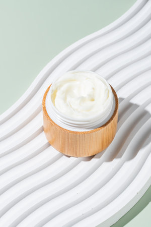 Jar with creamy cosmetic product, cream on white tray on green background. Unbranded package with antioxidant cream for self-care. View from above.の写真素材