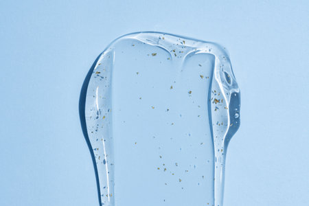 Close-up, transparent 24k gold serum drop smear on blue background, showcasing squeezed clear...