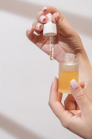 female hand with Dropper of essential oil, aromatherapy essence, beauty serum or medicinal liquid on light background with shadows. Unbranded bottles for your designの写真素材