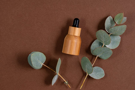 Blank bamboo essential oil bottle with pipette on brown background decorated eucalyptus leaves. Skin care concept with natural cosmeticsの写真素材