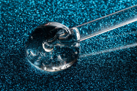 close up macro of pipette dropper with liquid serum on a glittering blue background luxury serum conceptの写真素材