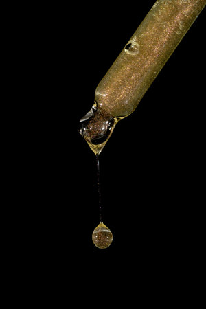 Bottle pipette dropper close up and Liquid yellow-orange shimmering retinol or vitamin c gel or serum on a black backgroundの写真素材