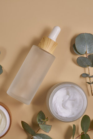 Set of beauty products in glass and bamboo bottles on beige background surrounded by eucalyptus leaves. Skin care set for daily routine. Mockup for designersの写真素材