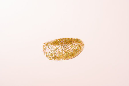 golden glitter gel smear on pastel pink background. Glistering particles on liquid. Swatch sample