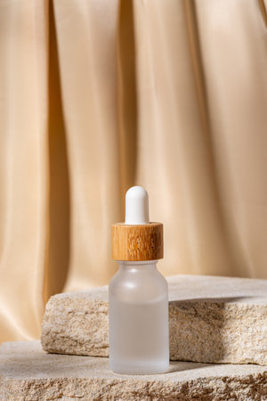 matte glass cosmetic bottles with a bamboo dropper cap on a beige background with stones and textile drapery. Natural cosmetics concept, natural essential oil and skin care productsの写真素材