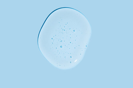 Close-up shot of blue liquid cosmetic gel drop or serum makeup swatches with a glossy, shiny texture on a smooth blue background.の写真素材